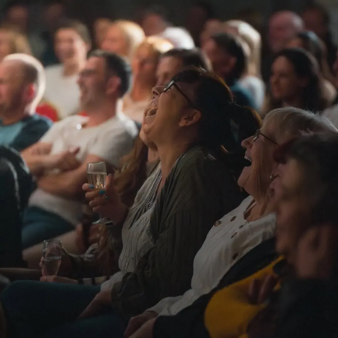 Audience members reacting from the side of a comedy room.