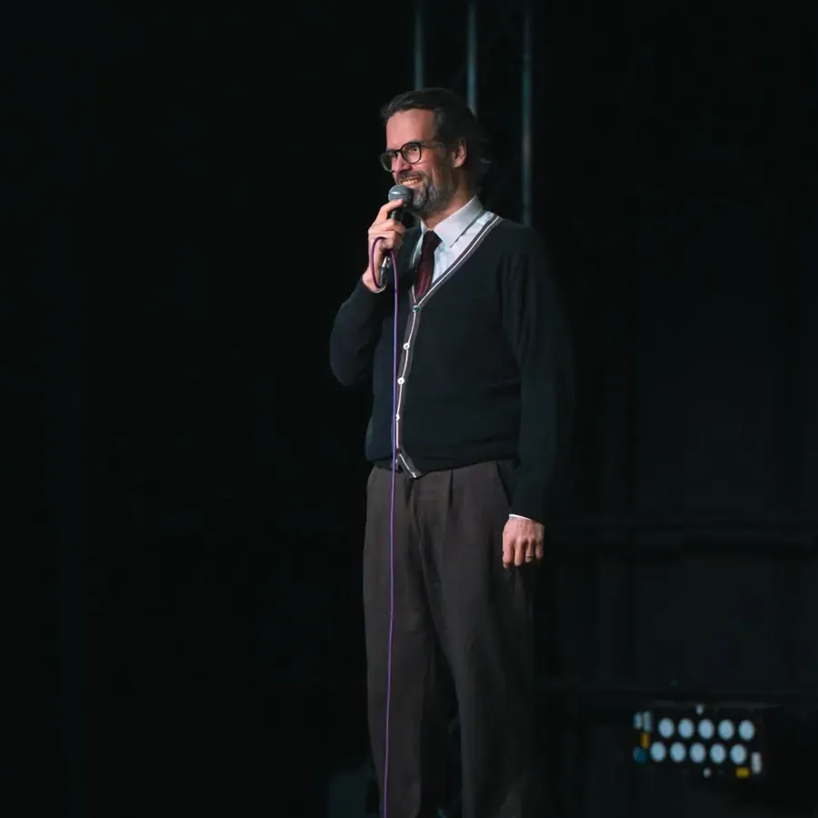 A comedian performing on a darkened stage with a microphone.