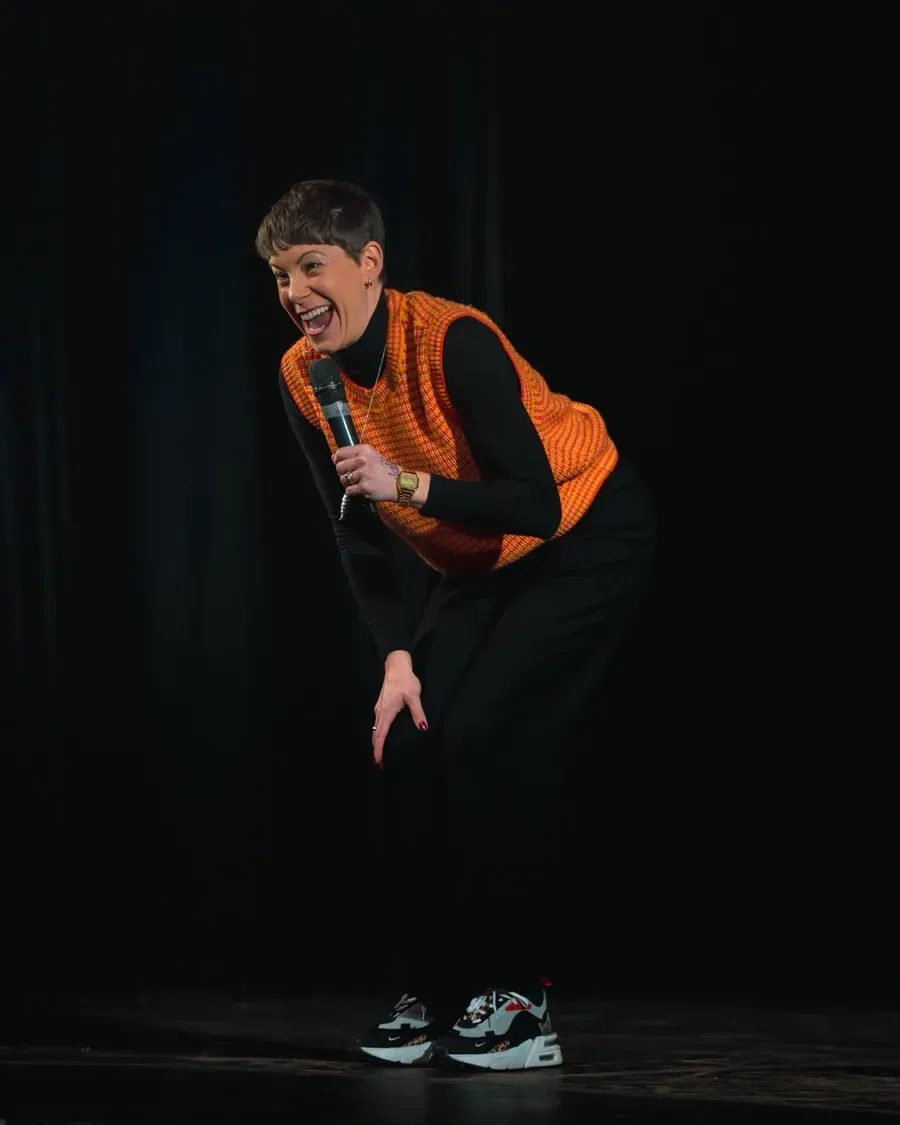 A comedian leaning towards the audience with a microphone.